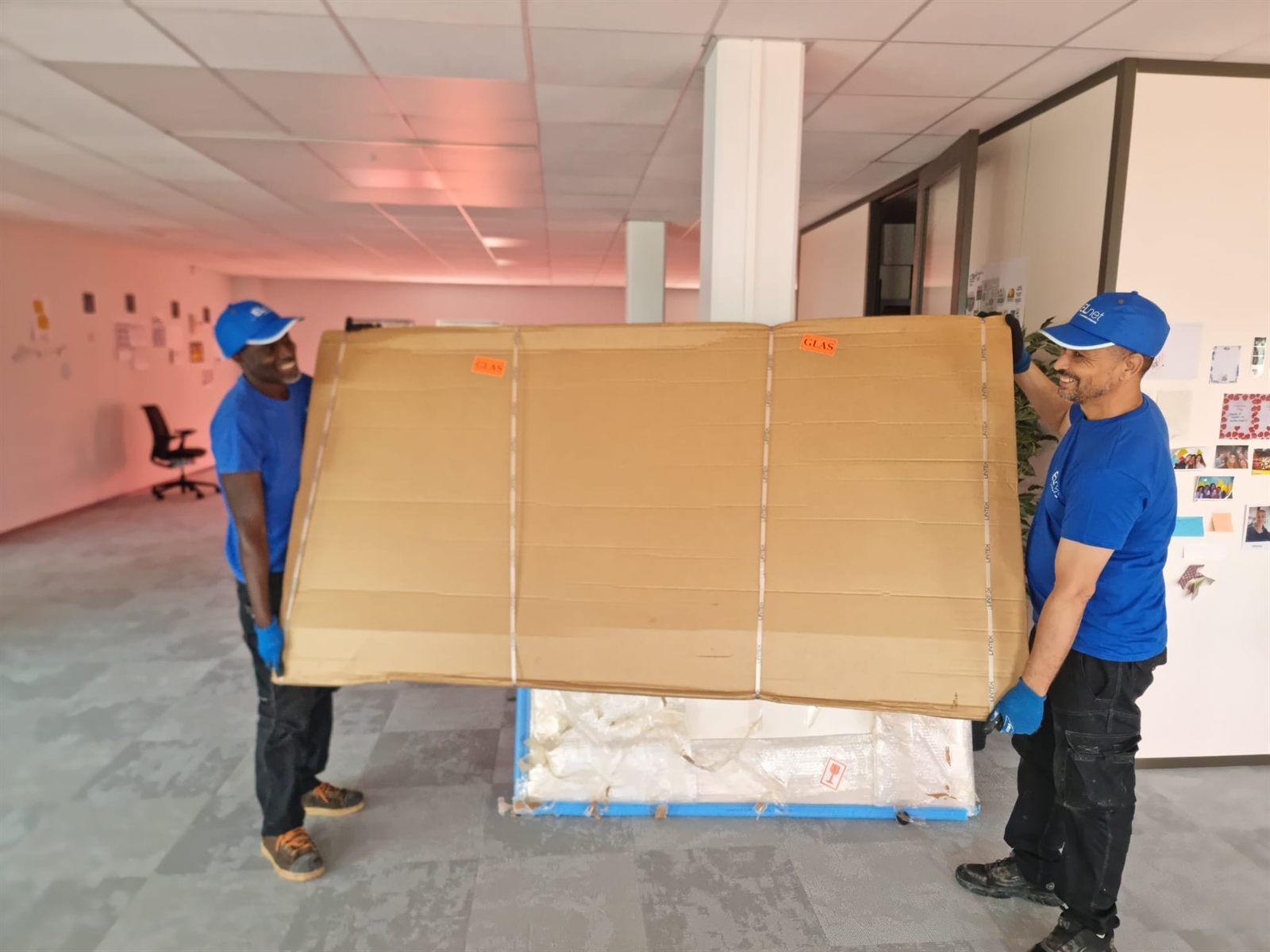 Deux équipiers ELnet portant un colis volumineux et fragile dans des bureaux